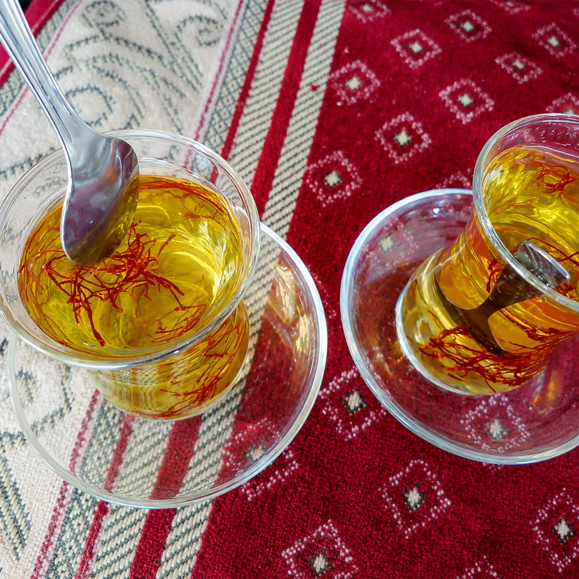 Two glass cups of freshly brewed saffron tea on a Herati carpet